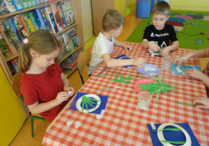 Trójka dzieci naklejają zielone papierowe łodygi na kartkę.